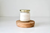Candle labeled 'Applewood Cinnamon' on a wooden coaster with a white background